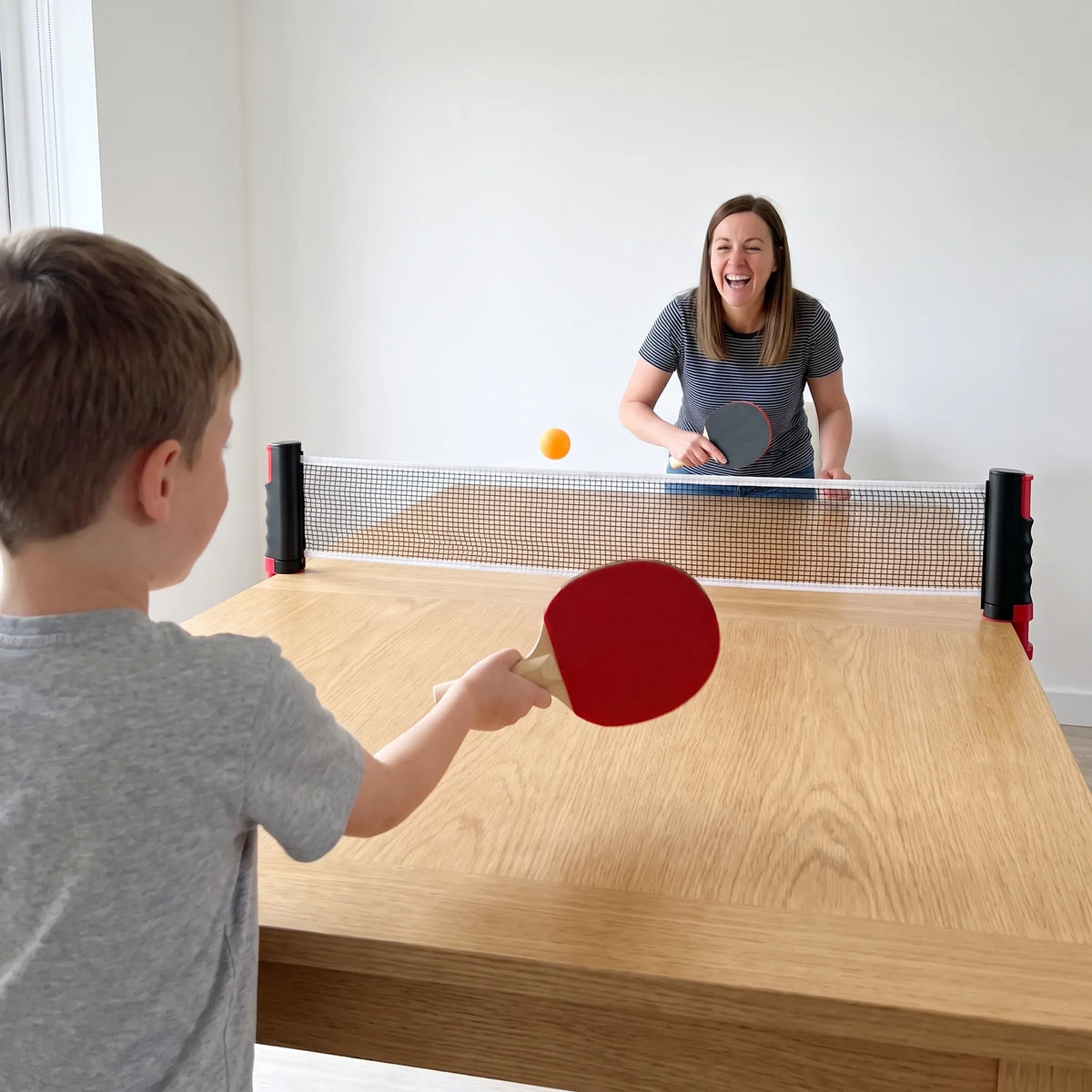 Boy and mom play ping-pong on either side of the net at the dining table